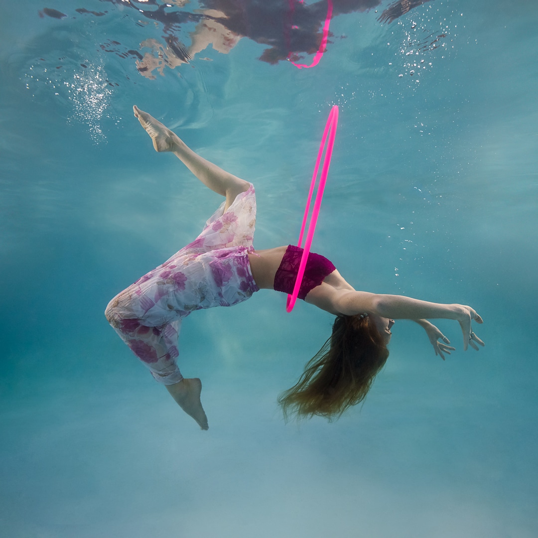 woman wearing pink and purple, hula hoop somersault dancing underwater