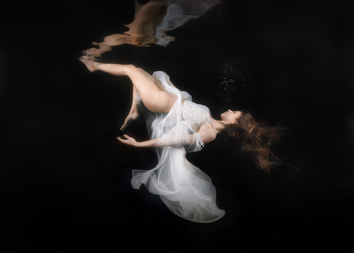 woman in white floaty gown, sinking underwater, black background, long hair, dreamlike