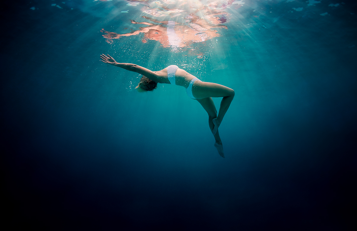 woman in white bikini underwater floating up to the surface, with sunbeams and reflections